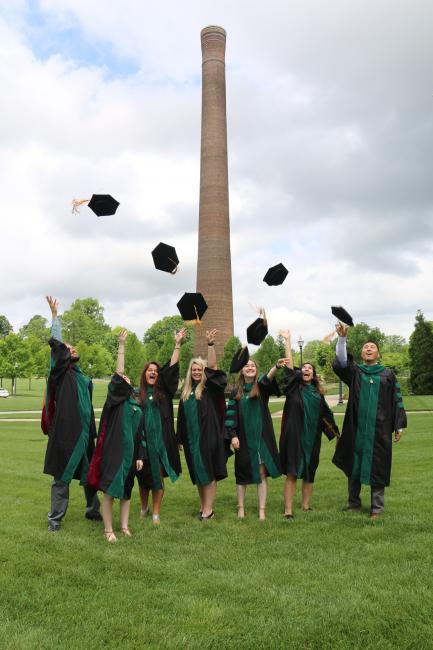 СƵ Carolinas graduates throw their caps into the air in front of the historic campus smoke stack